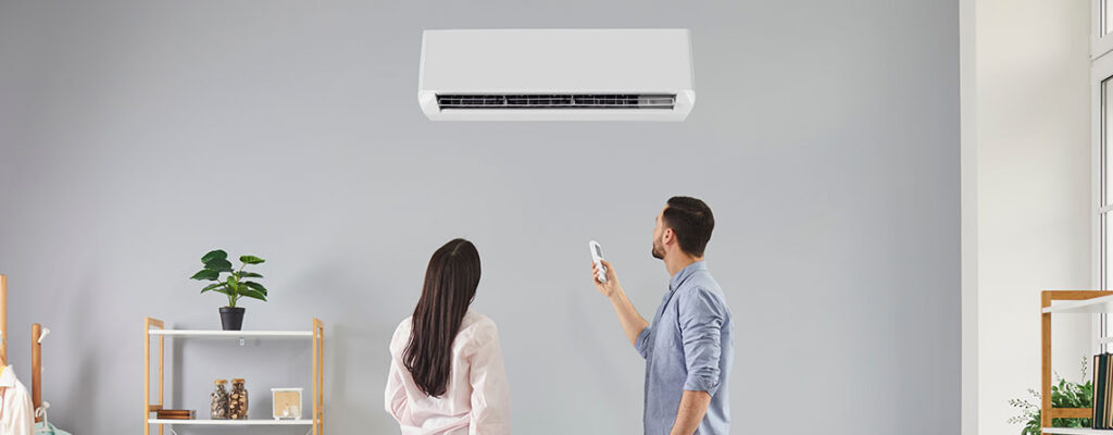 Man adjusting the temperature of a split type air conditioning unit installed in a cosy room