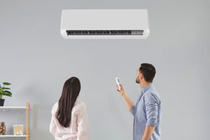 Man adjusting the temperature of a split type air conditioning unit installed in a cosy room